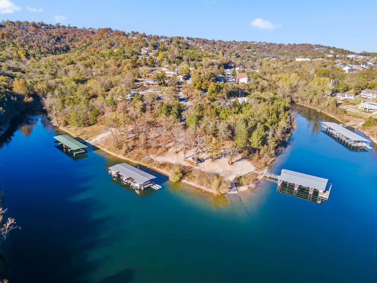 A panoramic view of calm blue lake waters bordered by wooded hills and dotted with wooden docks and hillside homes. The lighting suggests either misty early mornings or tranquil dusk, ideal for romantic shoreline strolls or connecting with nature.