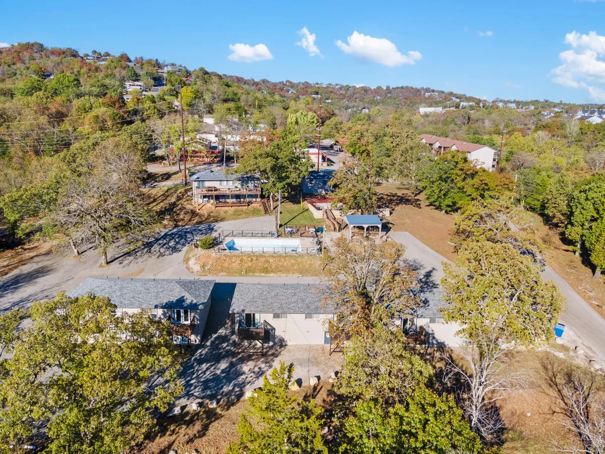 The image displays the main building surrounded by mature trees and nearby recreational areas. There's a welcoming vibe, with spacious outdoor areas suitable for gatherings, play, or relaxation.