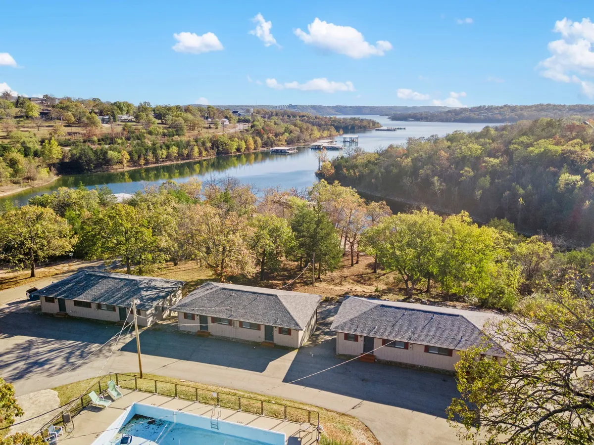 This exterior image shows a sparkling swimming pool with a row of cozy cabins and Table Rock Lake visible in the background, framed by trees. The pool area looks inviting for families, and the backdrop of the lake emphasizes the connection between resort amenities and outdoor adventure.