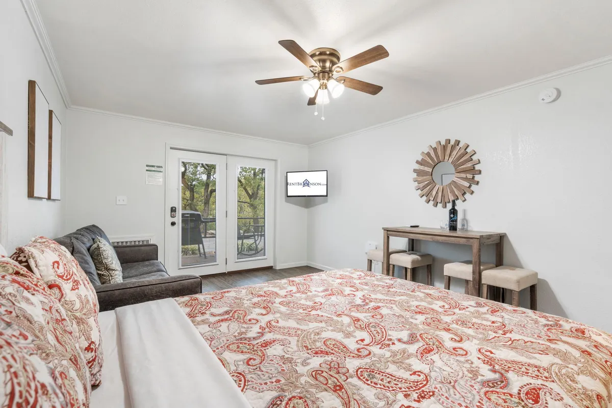 An interior view featuring a bed with patterned bedding, a cozy seating area, TV, and double doors that lead outside, hinting at direct access to fresh air and outdoor space.