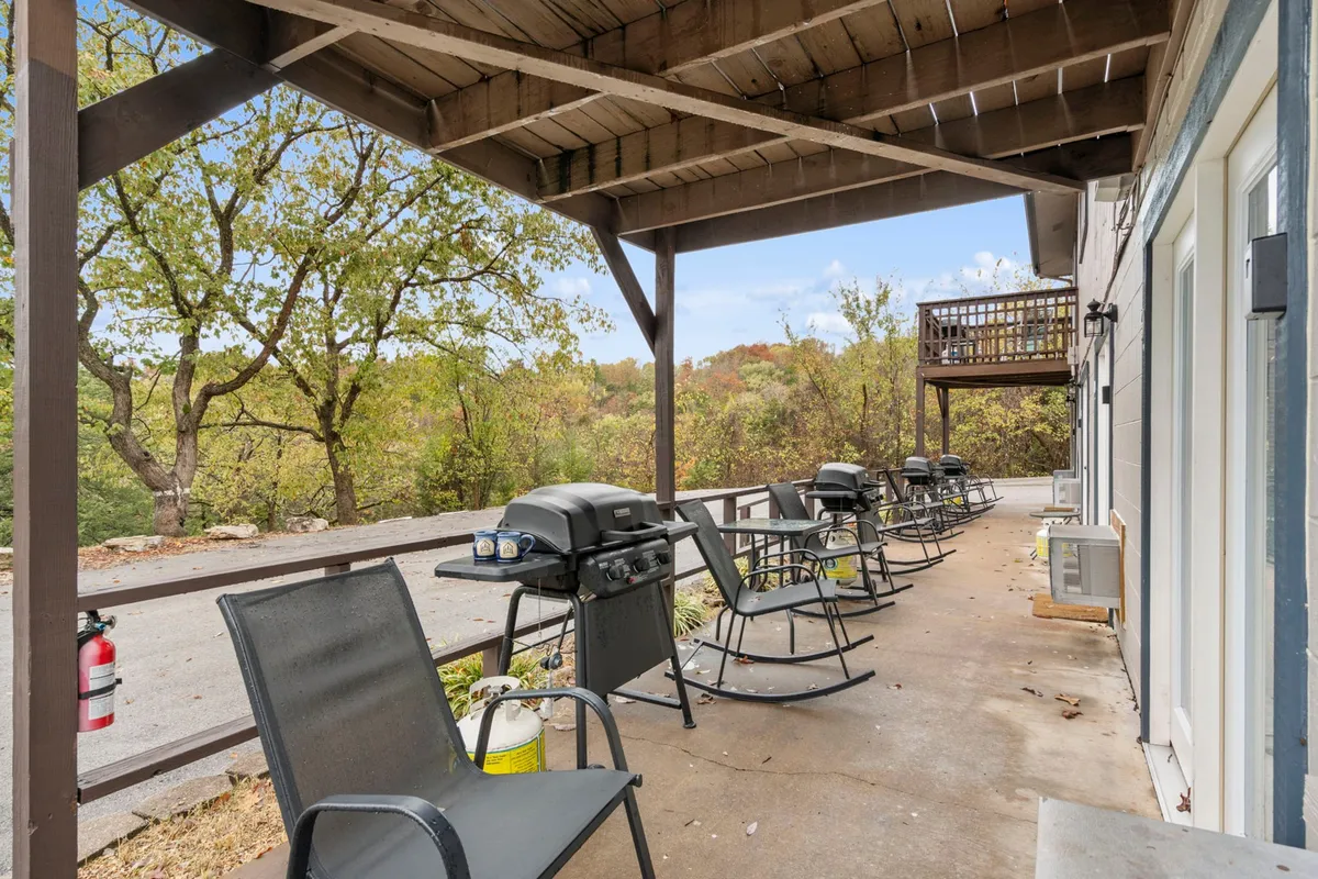 A cozy outdoor communal deck space featuring grills, wooden rocking chairs, and sturdy wooden beams. The scene is set for group gatherings or intimate evenings, with the soft glow of sunset hinting at relaxing nights under the stars.