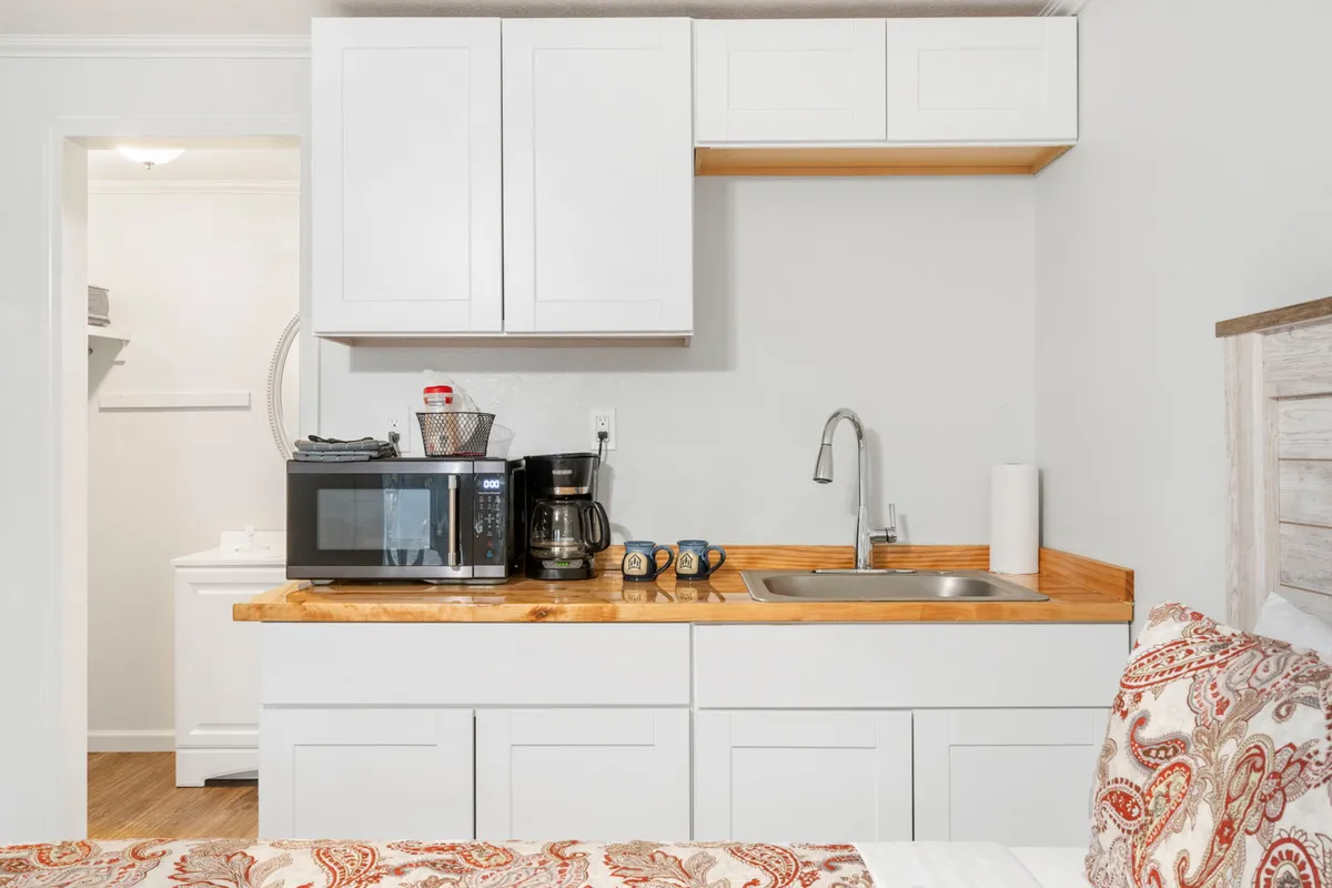 A close-up of the kitchenette area, featuring a coffee maker, microwave, and sink. The setup is compact yet functional, evoking the ease of preparing snacks or breakfast within the studio.